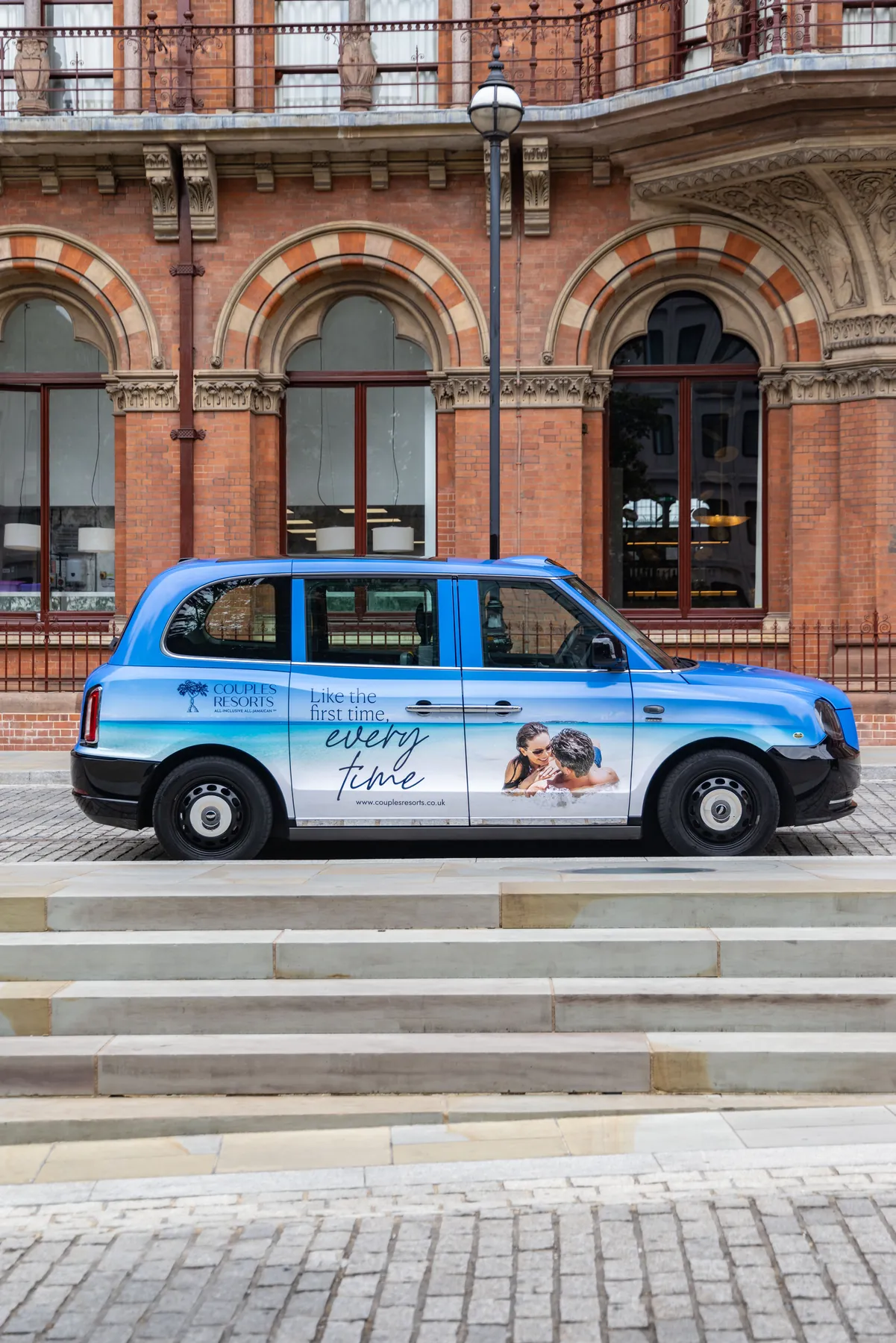 Blue taxi in Couples Resorts livery parked side-on beside red-brick arches