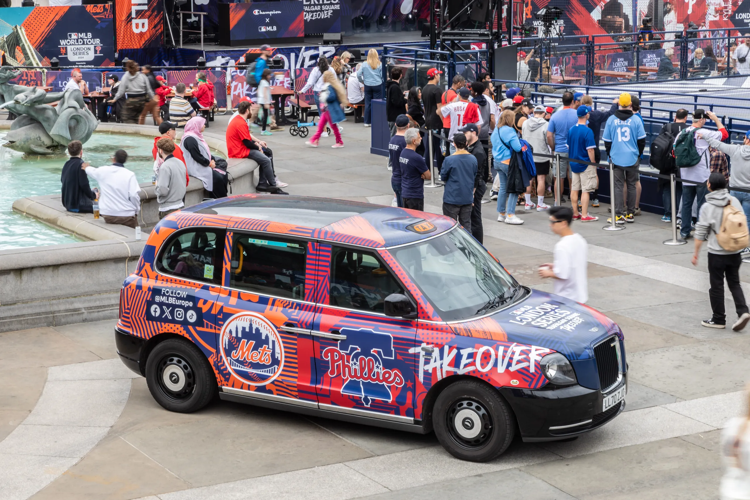 Taxi in New York Mets and Philadelphia Phillies livery in Trafalgar Square, with crowds behind